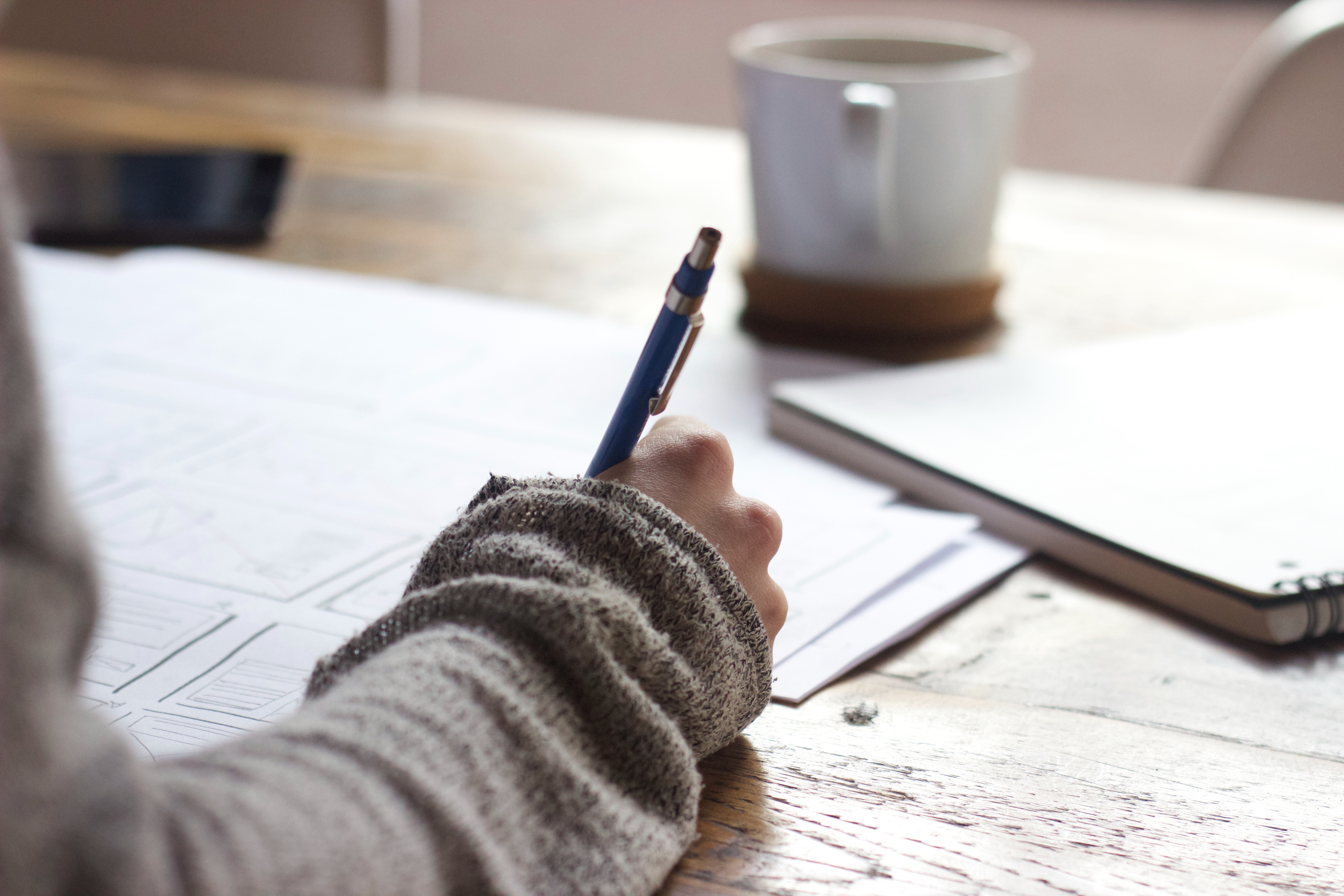 A student makes notes on paper, a cup of coffee in the background