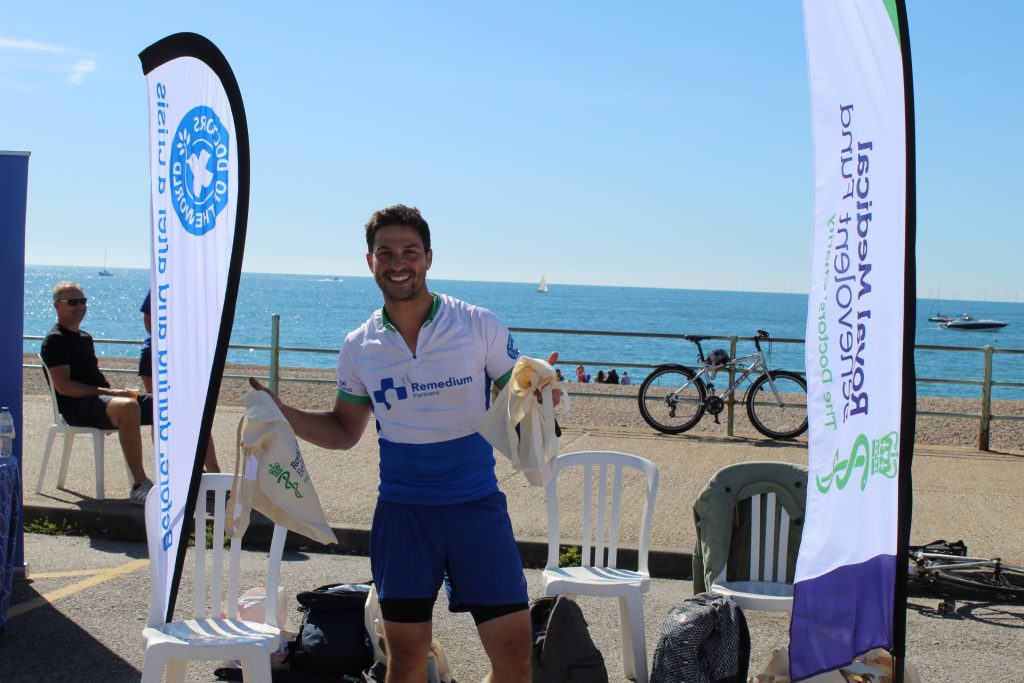 Cyclist Oliver Jansen smiling and holding a goodie bag in the sun on Brighton seafront