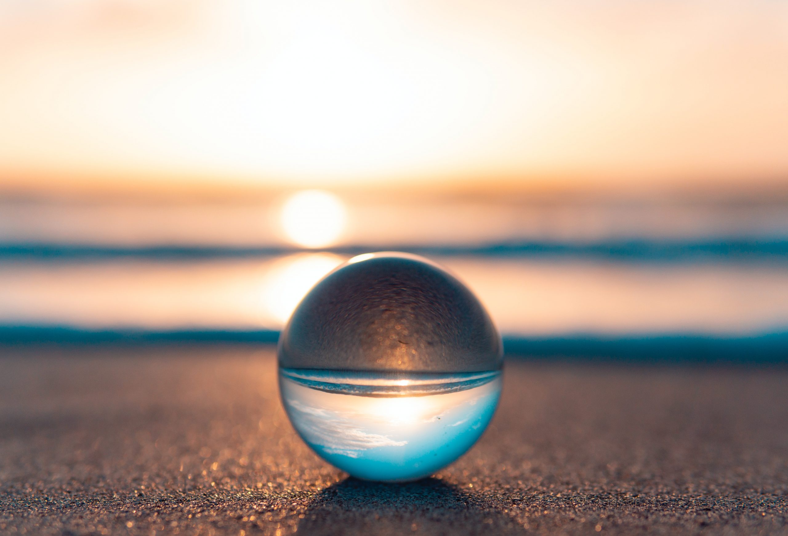 A clear glass ball resting on a beach, the sunset reflecting through it.