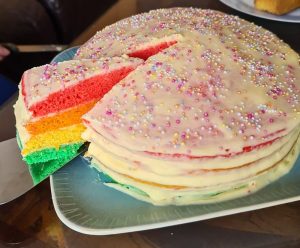 A slice being cut from a cake with rainbow coloured layers