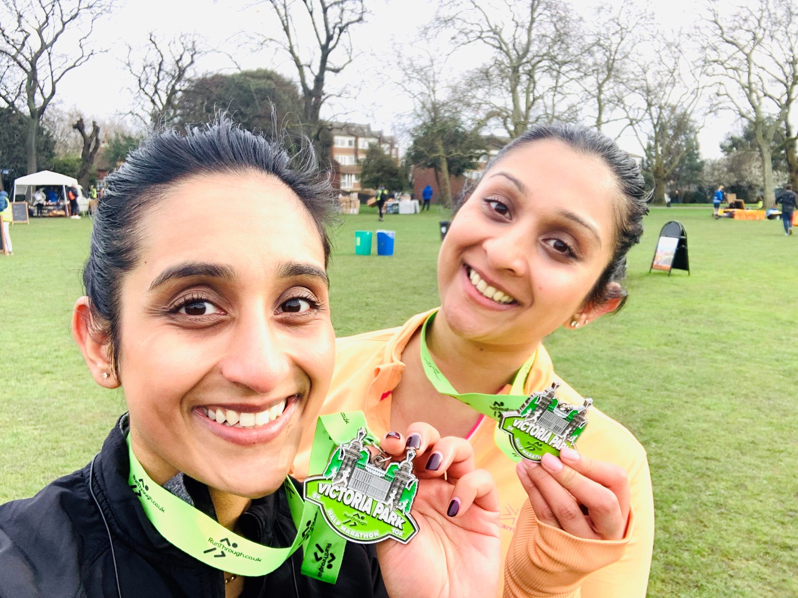 Two women in a park, smiling and holding medals from a fundraising running challenge