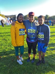 Thando and two friends standing and smiling in a field, wearing running numbers