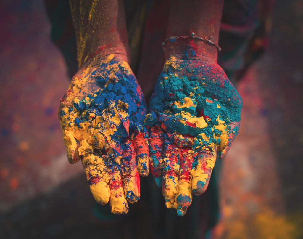 Hands cupped and carrying different coloured powder (yellow, blue, teal, pink)