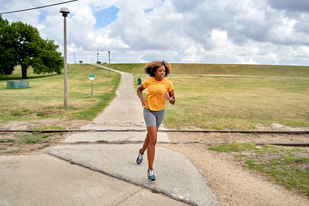 Girl running in a yellow t-shirt and grey shorts on a path 