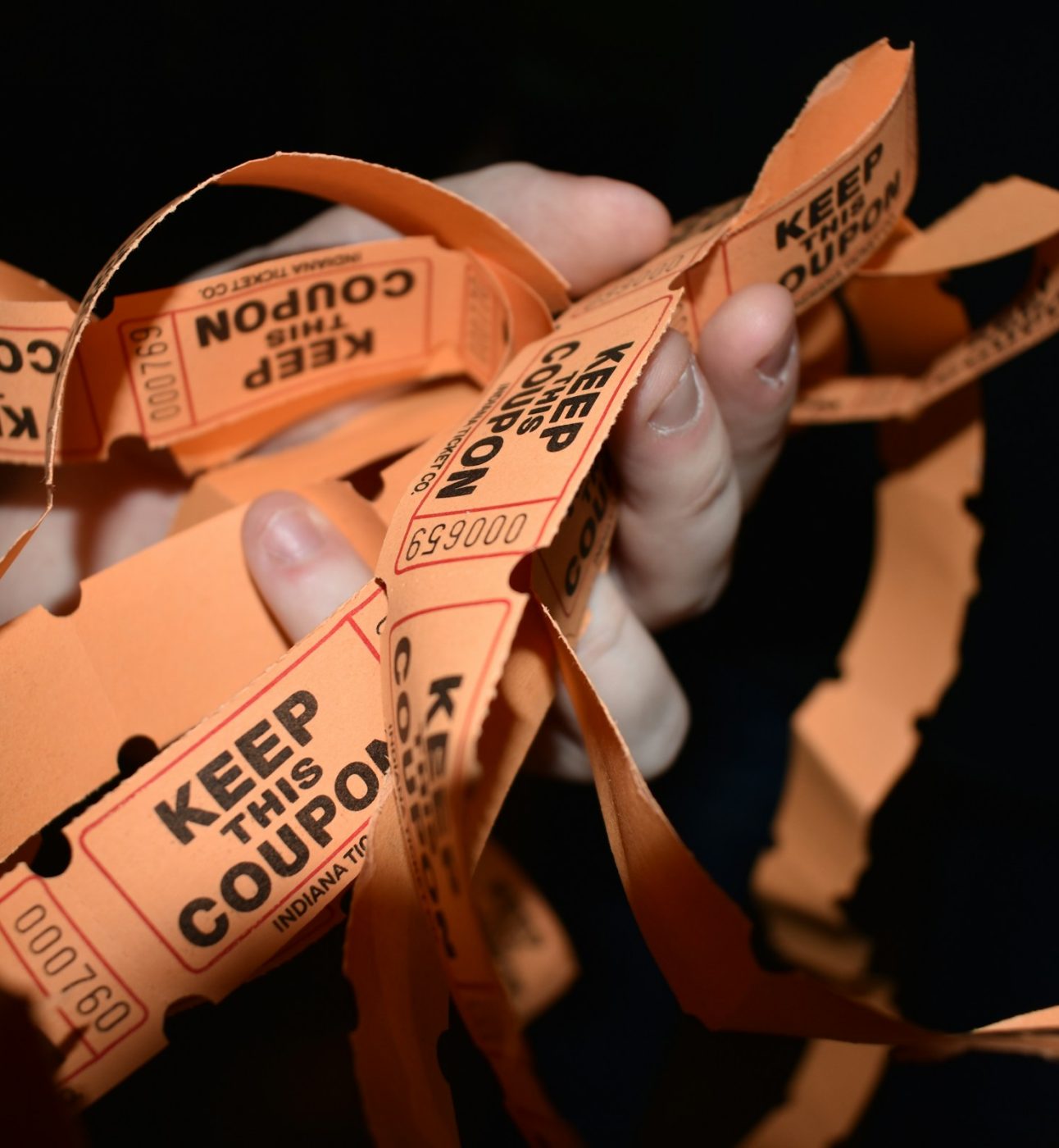 A hand holding a pile of orange raffle tickets saying 'keep this coupon' on each one