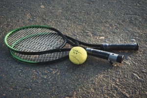 Two tennis racquets and a ball sitting on the ground