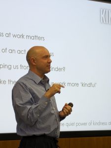 Graham Allcott, a shaven-headed white man in a blue shirt, is giving a presentation. His slides are on a big screen behind him.