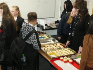 Cakes displayed on a table with students gathered around