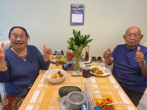 Rosie's friends and family- a man and a woman, sat at a table with plates of food, smiling and giving a thumbs up.