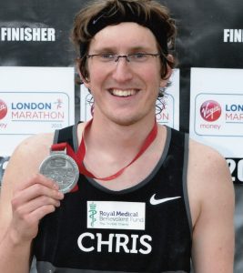 Man in a running vest with his name printed "Chris", holding a medal