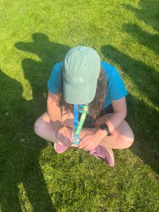 Megan sat in a field, wearing t-shirt and shorts and a cap, looking down at her medal