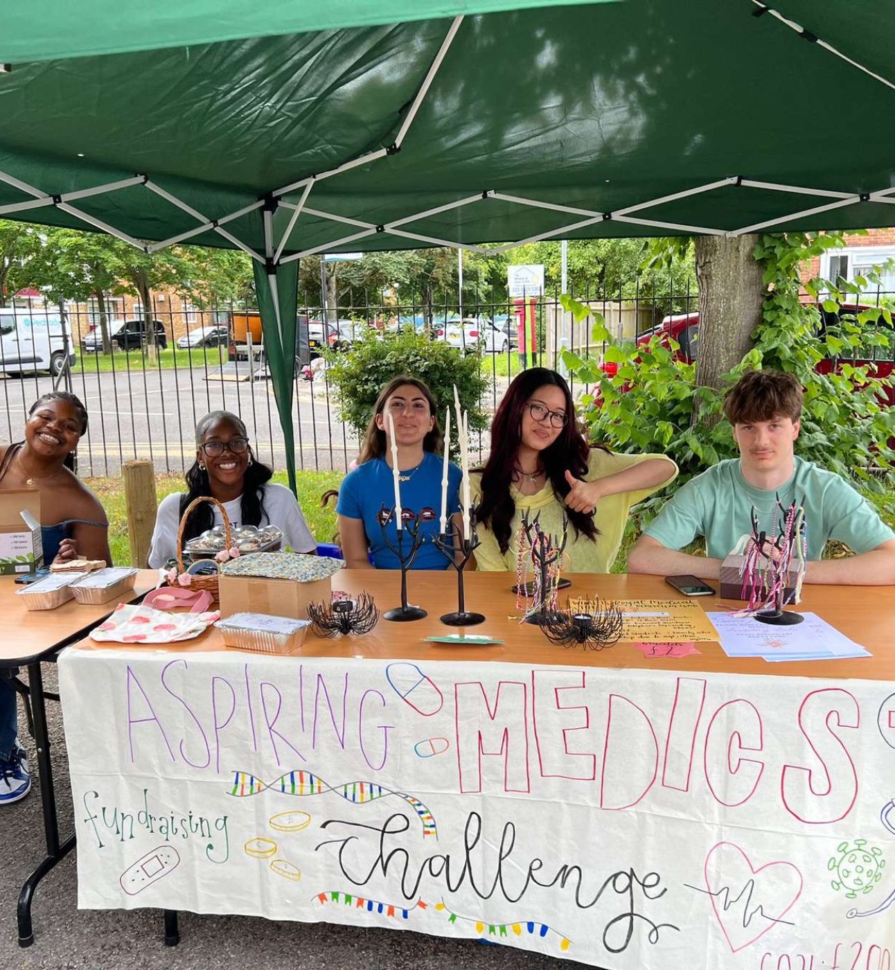 A group of five students sat behind a table with candles and bracelets displayed. There is a sign on the front of the table that reads 