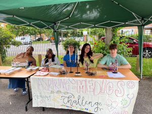 A group of five students sat behind a table with candles and bracelets displayed. There is a sign on the front of the table that reads "aspiring medics challenge."