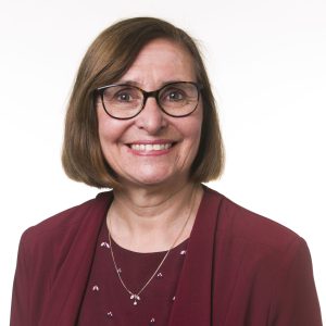 A photograph of Jane Dacre, smiling. She is a white woman with shoulder-length brown hair and glasses. She's wearing a maroon jacket and top.