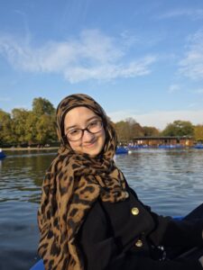 Sumaiya, sat smiling outside, in front of a lake