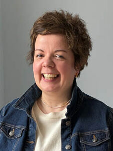 A head-and-shoulders photograph of Dr Zoë Barron, smiling. She is a white woman with short brown hair, wearing a blue denim jacket over a white top.