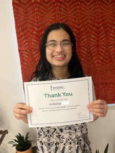 Asmita, smiling and holding an RMBF certificate with her name on.